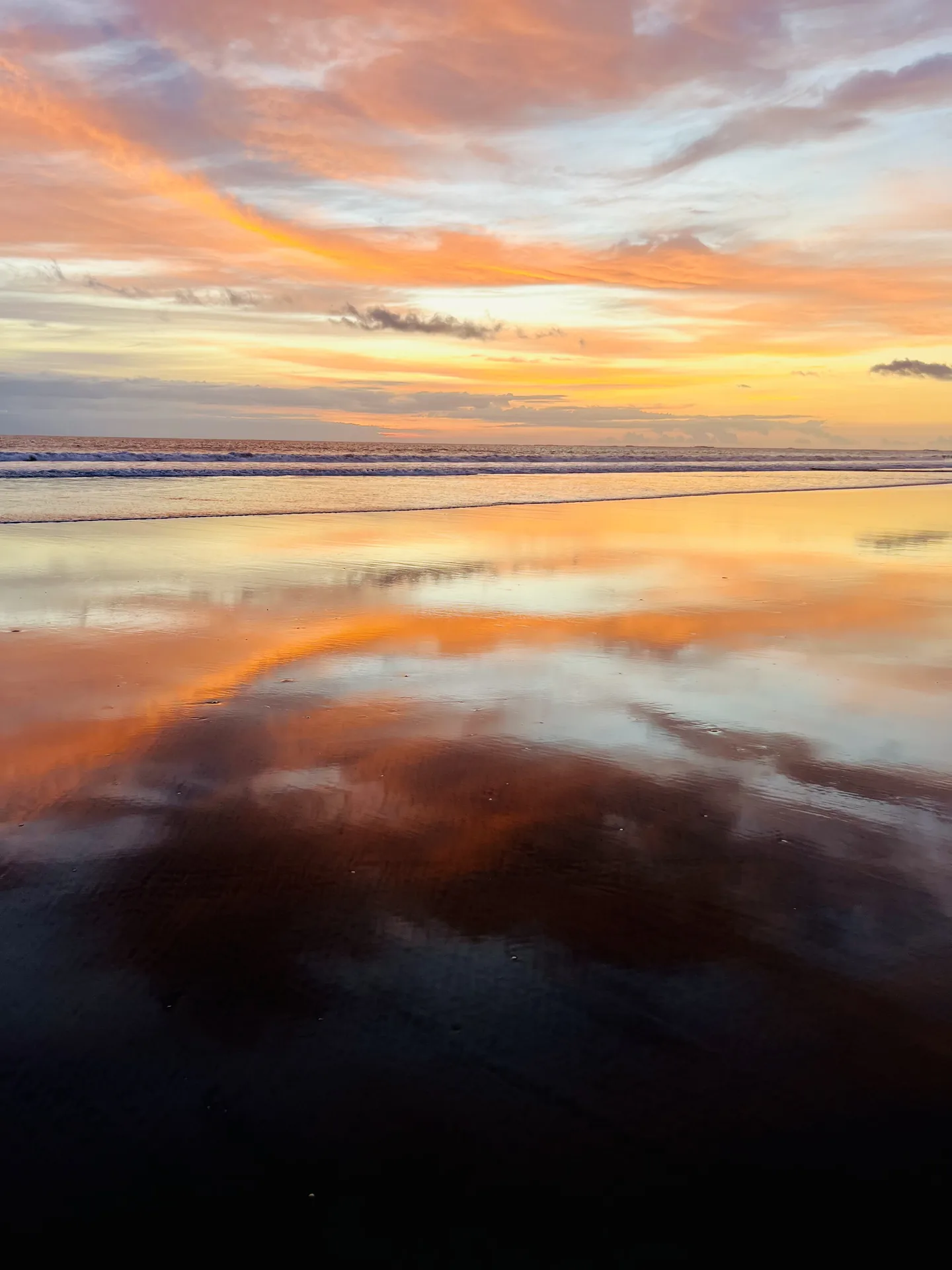 Orange clouds mirrored on the wet sand