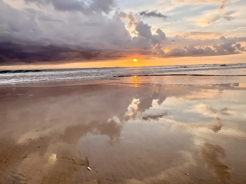 Clouds mirrored in wet sand at sunset
